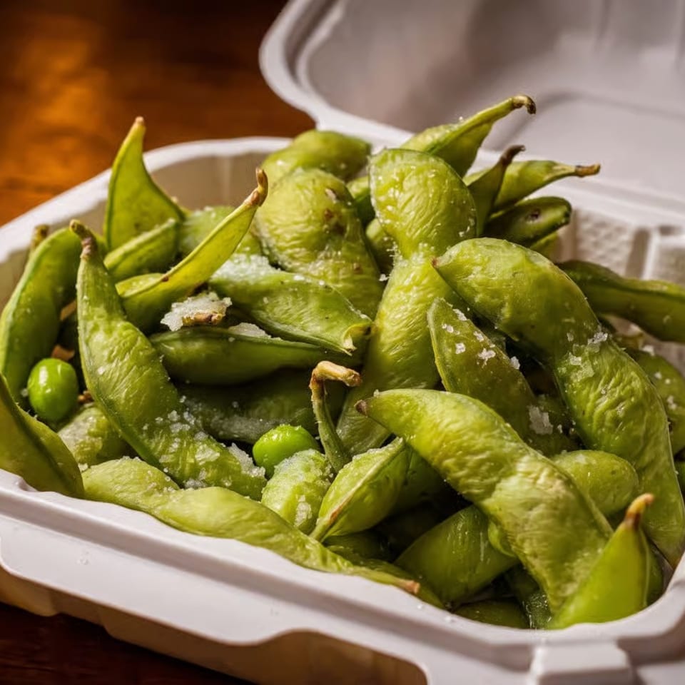 Salted edamame in a white takeout container on a wooden table.